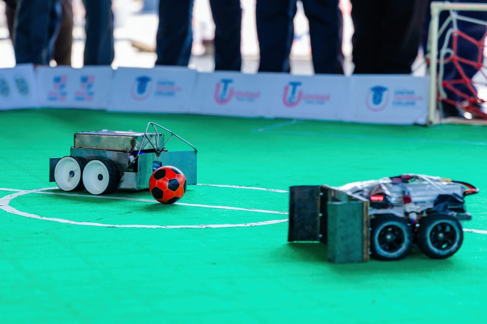 Two student-built robots playing robot soccer on a green field